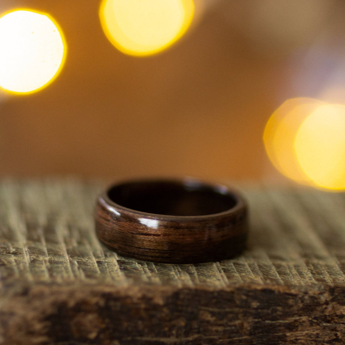 Polished dark wood ring crafted from ebony using bentwood technique, resting flat on rustic wood with soft golden lighting.