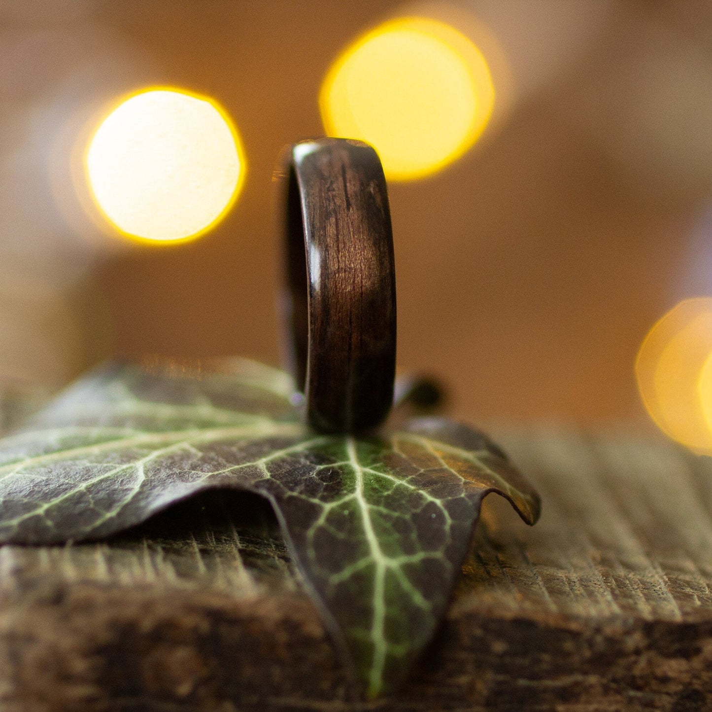 Minimalist ebony wood ring standing vertically on a leaf, showcasing its smooth grain and handcrafted finish.