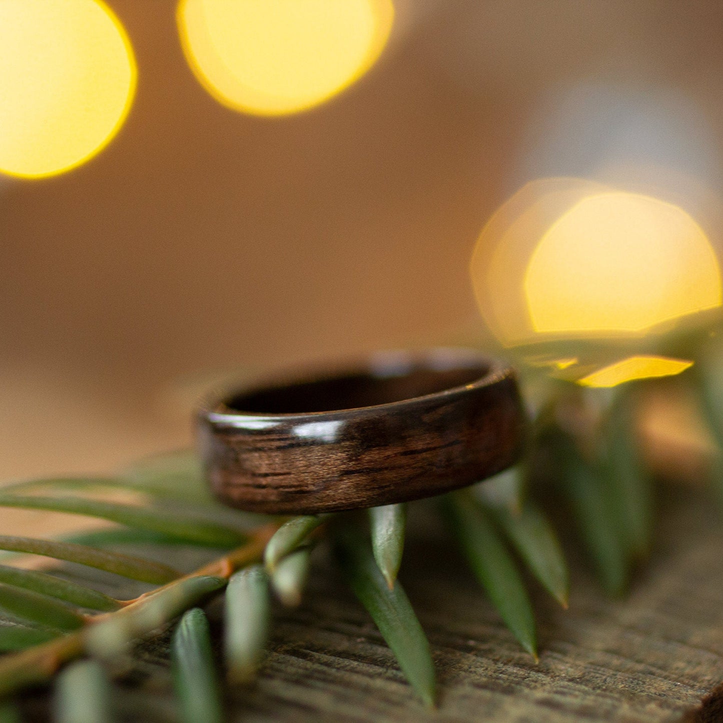 Dark wood ring made from ebony placed on pine needles, highlighting its natural texture and elegant curve.