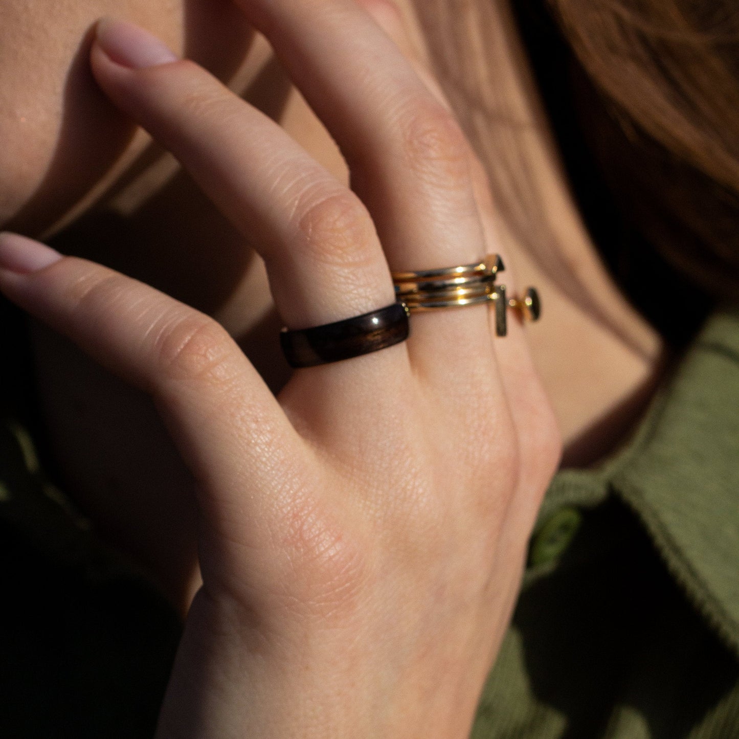 Ebony bentwood ring styled on a hand with gold rings, showcasing its deep color and smooth craftsmanship.
