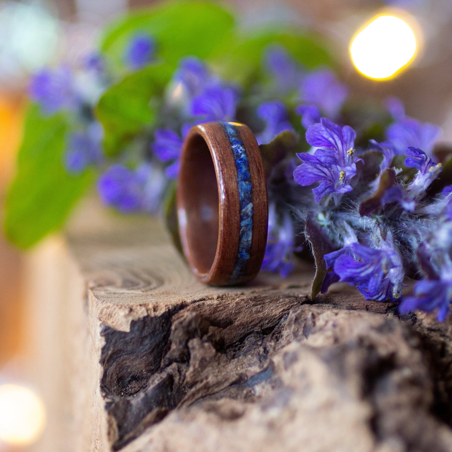 Makore and lapis lazuli ring resting on rustic wood, surrounded by purple blossoms.