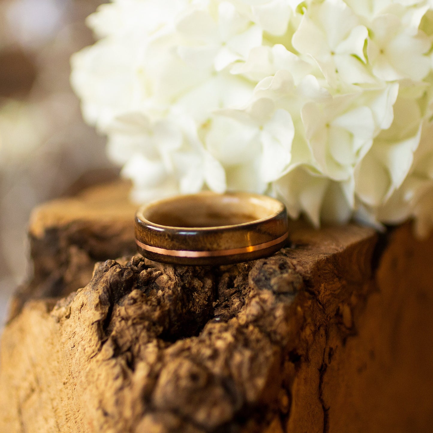 Flat-laying scorched ash ring with copper inlay, placed in front of soft white hydrangea bloom.