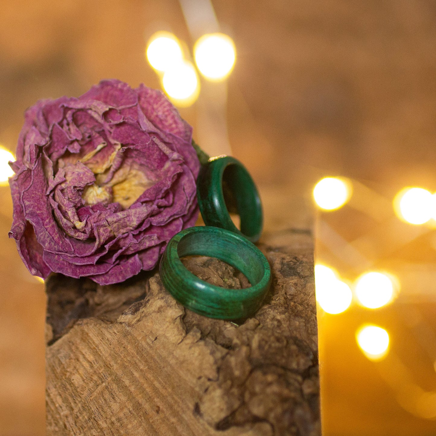 Hornbeam wood rings in forest green, styled beside a dried pink flower for a moody woodland vibe.