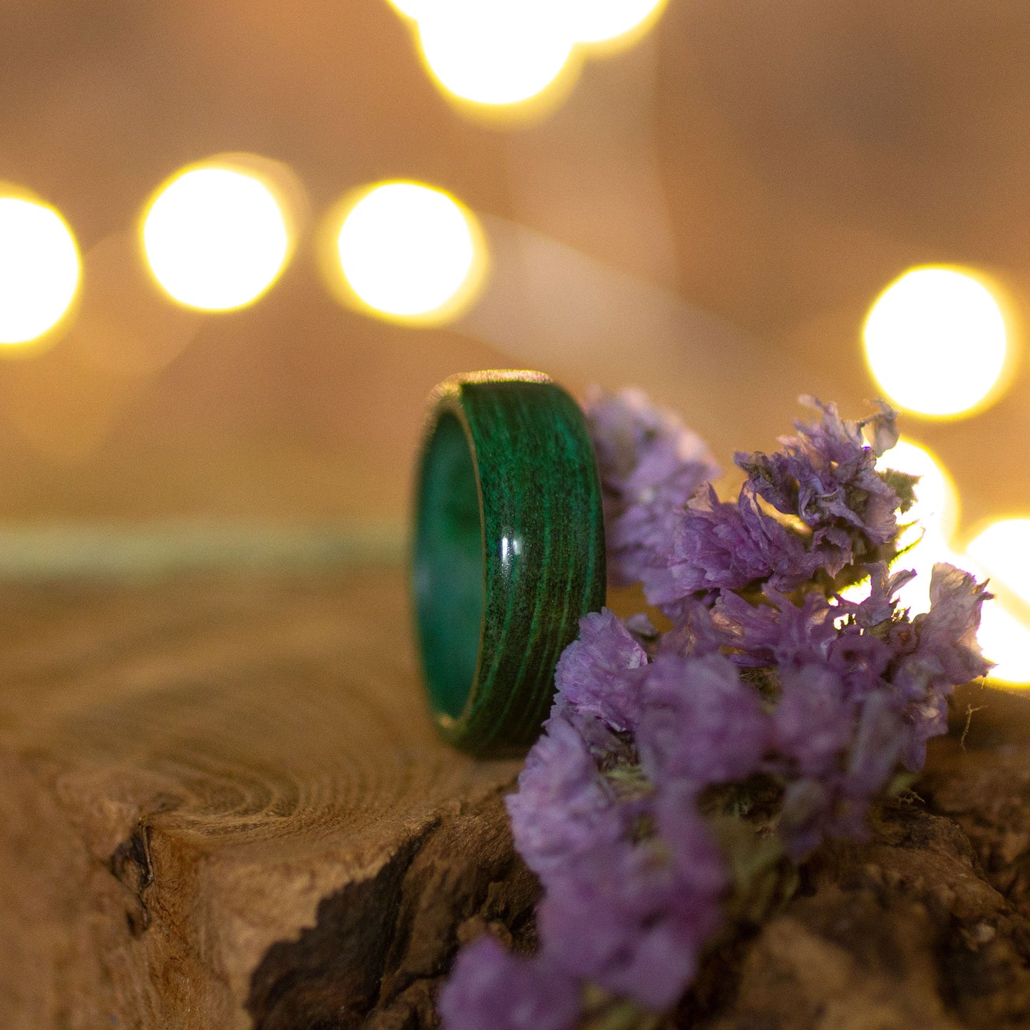 Green hornbeam wood ring resting beside soft purple blooms, set against a glowing background.