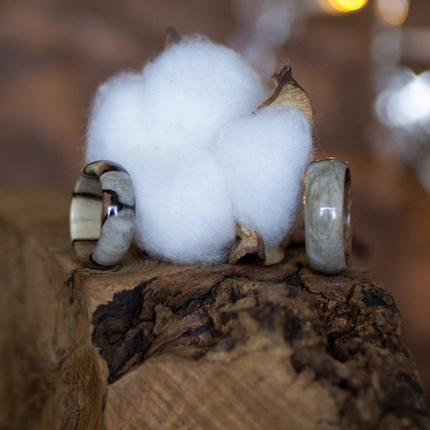 Two handcrafted birch wood rings with epoxy inlay beside cotton, styled against rustic wood and lights.