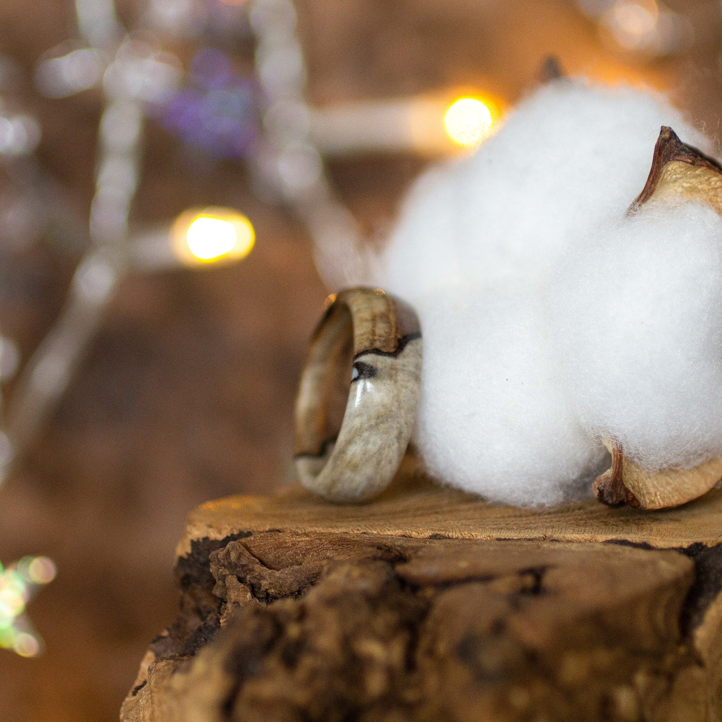 Side profile of birch wood and epoxy ring, placed on bark with cotton and fairy lights in background.