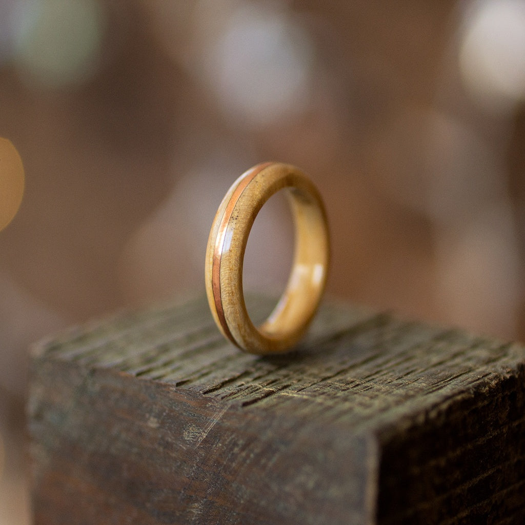 Vertical view of light ash and copper ring on textured wood, soft highlights accentuating warm tones.