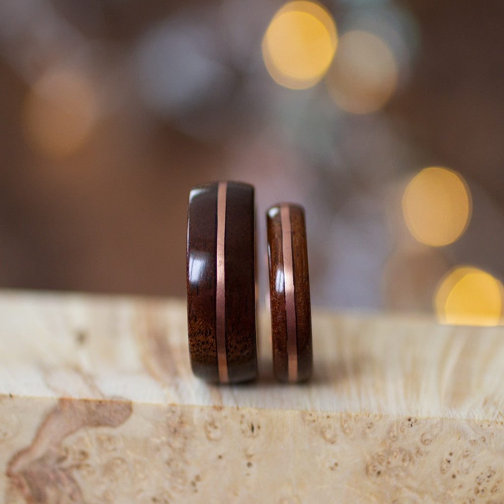 Side-by-side view of two mahogany rings with copper stripe, upright on beige stone background.