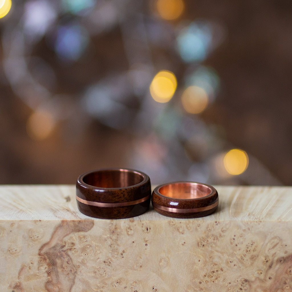 Pair of mahogany and copper rings resting on marble slab, with blurred festive lights behind.