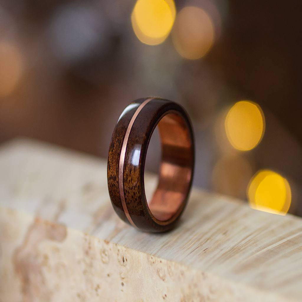 Mahogany wood ring with copper inlay, standing on marble-textured surface with soft warm lighting.
