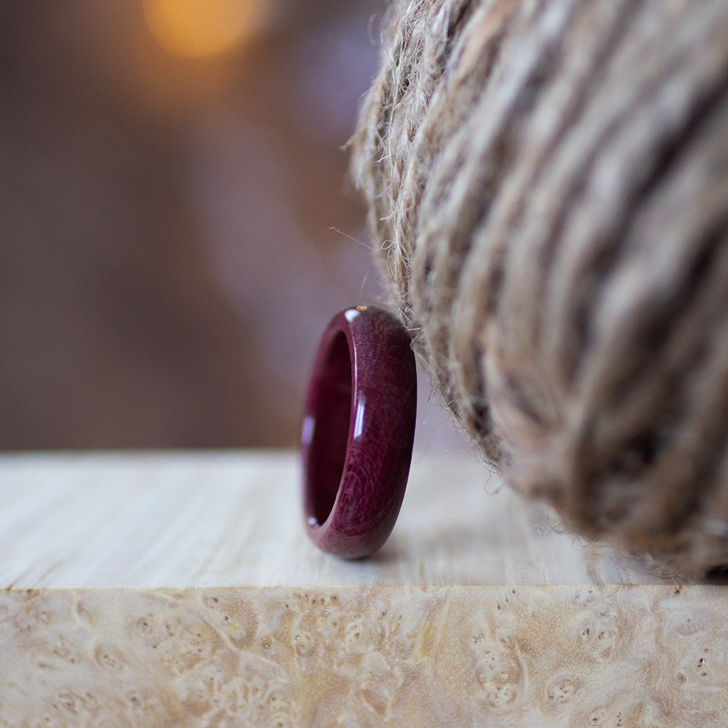 Side view of Purpleheart wood ring near rustic twine, set on marble-like surface in soft light.