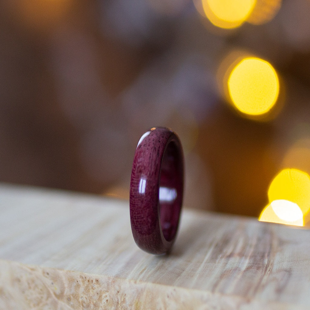 Purpleheart wood ring standing on pale wood surface, showcasing rich burgundy tone and polished finish.