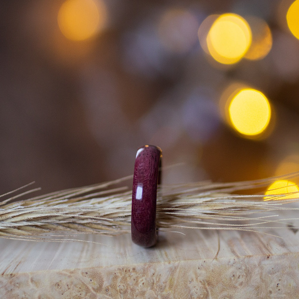 Purpleheart ring standing beside dried wheat stalk, warm ambient background creating cozy mood.