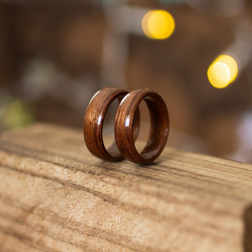 Pair of makore wood rings resting on smooth wooden surface, showcasing deep reddish grain and sheen.