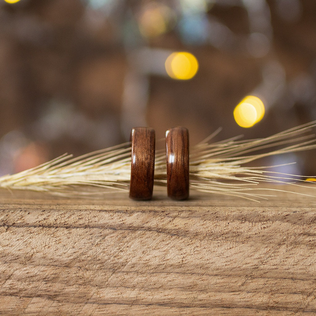 Makore wood rings paired together with dried grass accent, set against a softly lit wooden base.