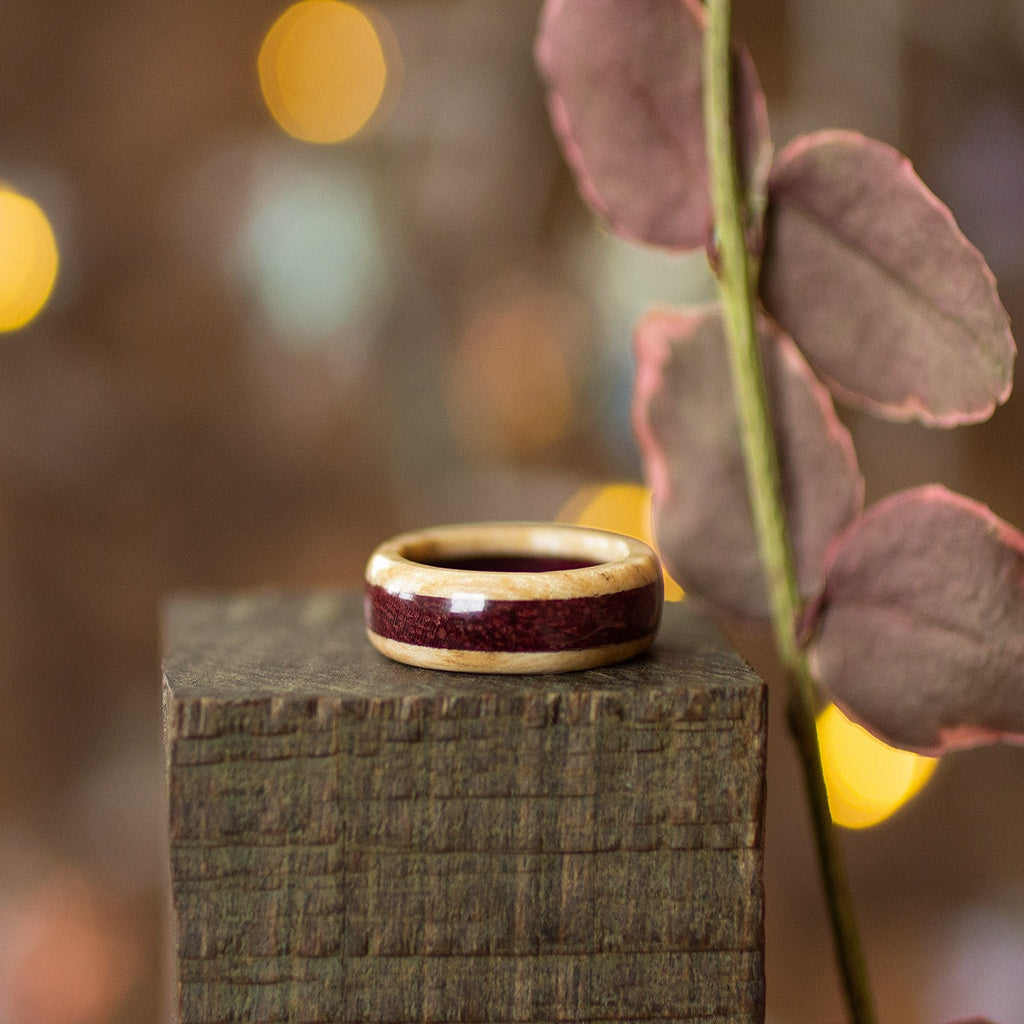 Flat-laying ash and Purpleheart ring with eucalyptus sprig, styled on dark wood in cozy lighting.