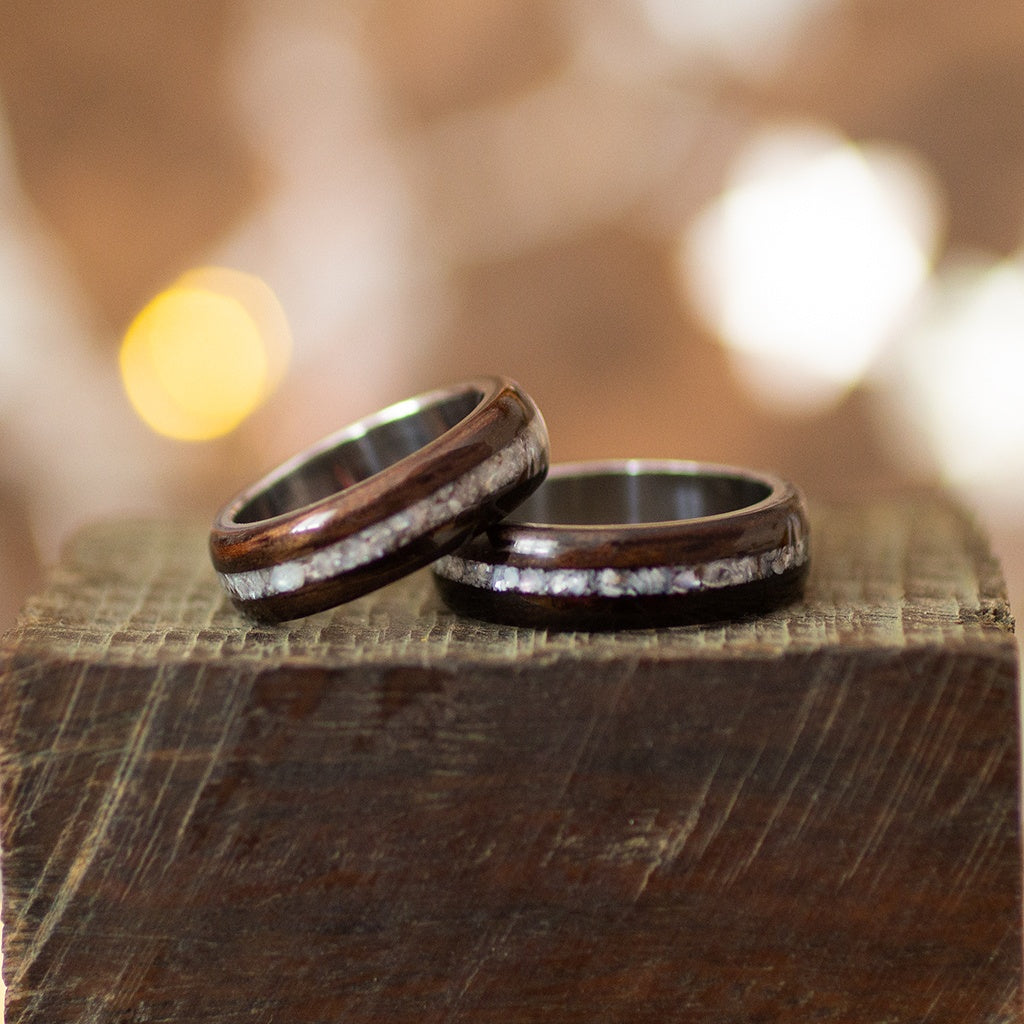 Pair of ebony rings with shimmering pearl inlay, placed flat on dark wood surface.