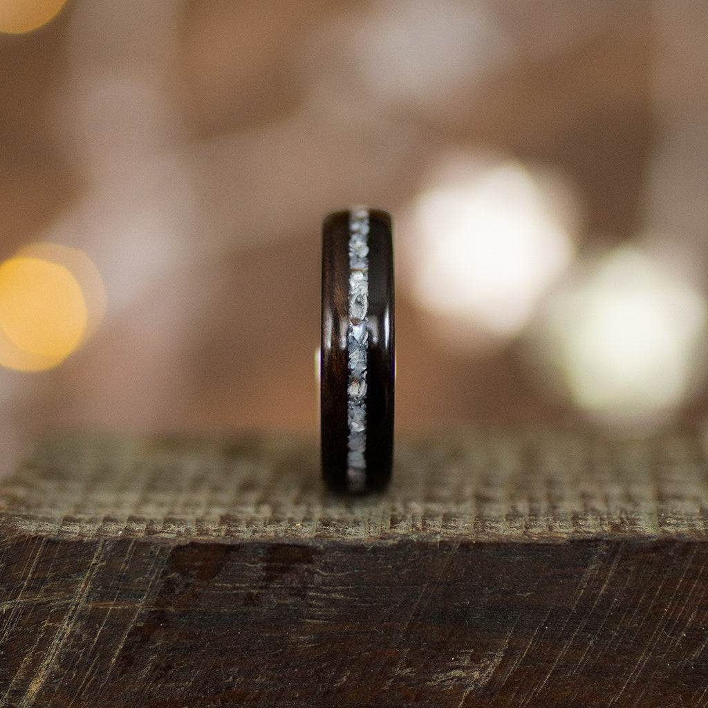 Side view of handcrafted ebony ring with iridescent crushed pearl line, propped on wooden block.