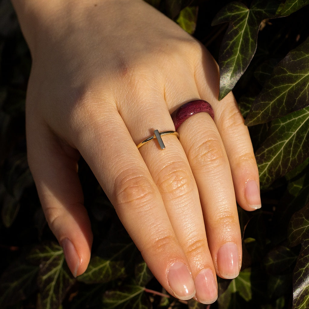 Hand wearing Purpleheart wood ring with deep plum color, resting among ivy leaves.