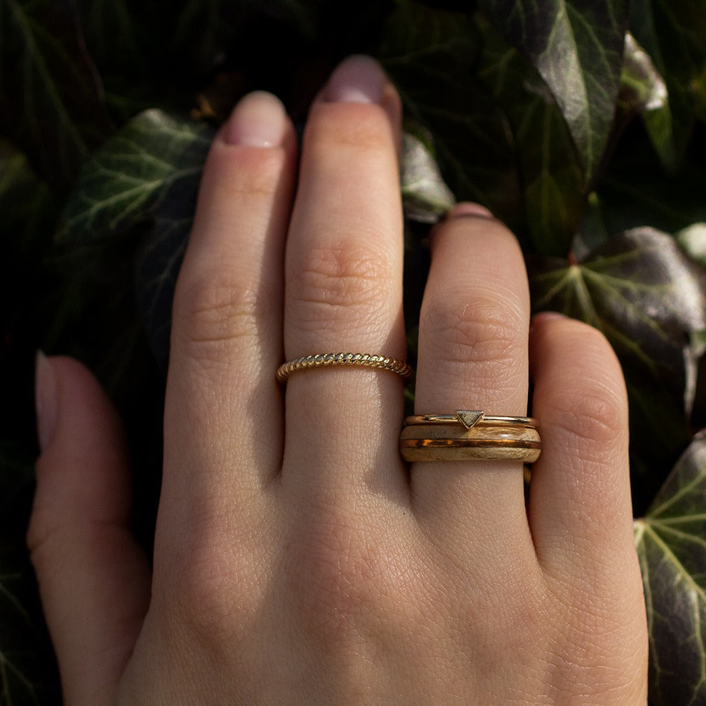 Hand wearing ash and copper ring, surrounded by ivy leaves and paired with gold band.