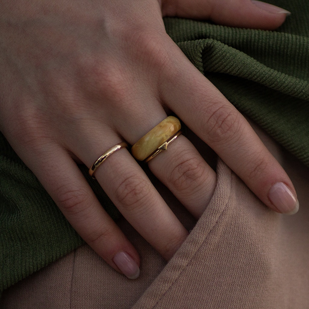 Close-up of hand with maple burl wood ring and gold accents, resting on green fabric for soft contrast.
