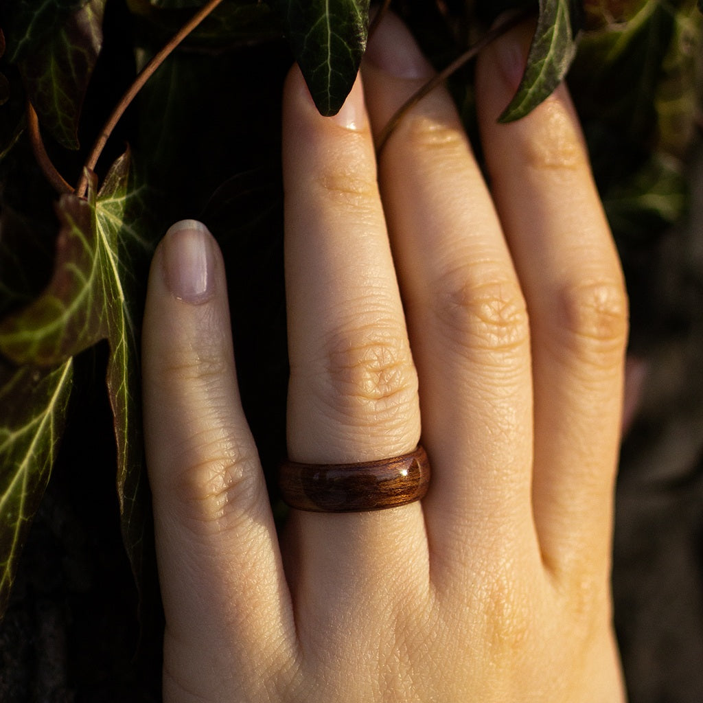 Close-up of hand wearing makore ring, framed by green ivy for a natural, earthy look.