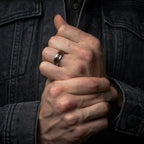Close-up of man's hands clasped together with a hammered wood inlay wedding ring on a dark background