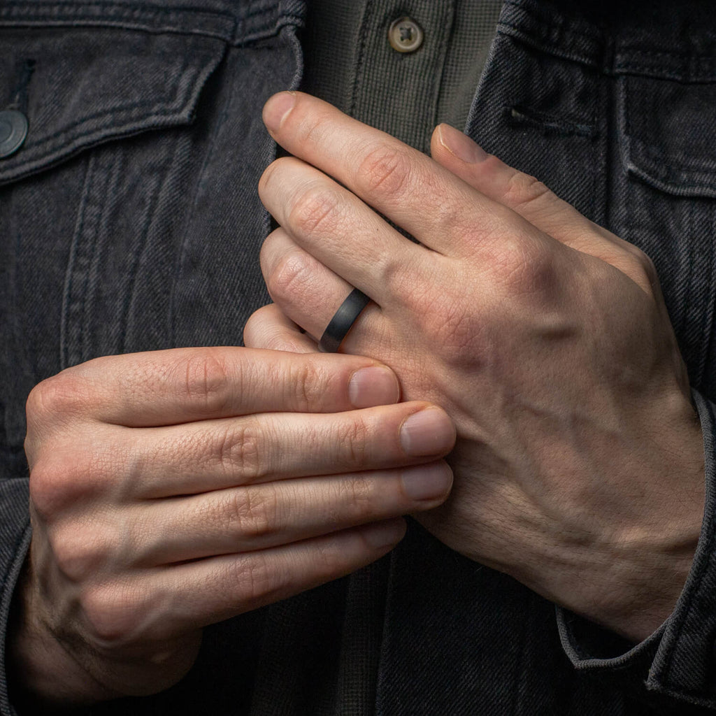Close-up of hands with a black wedding ring, wearing a dark jacket.