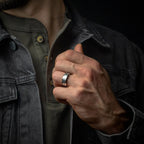 Person wearing a dark jacket with a close-up of a hand adjusting the collar, focusing on a silver tungsten ring.