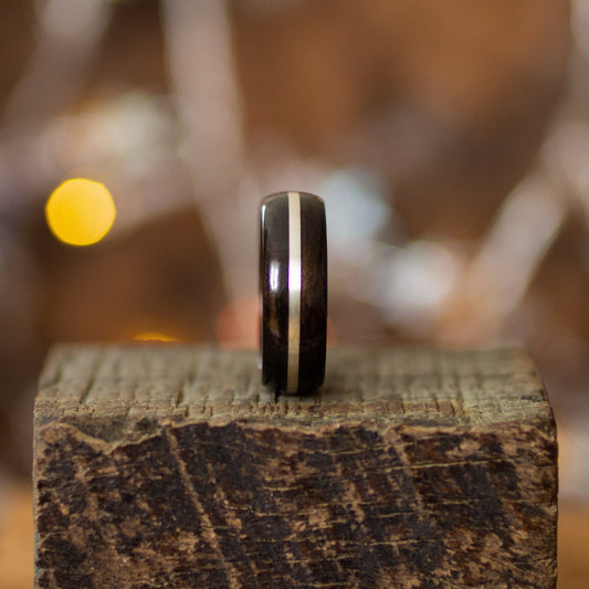 Ebony Wood Ring with Silver Inlay by Andrwood displayed vertically on rustic wood, showcasing its smooth finish and minimalist silver stripe.