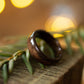 Handcrafted ebony wood ring resting on greenery, emphasizing its minimalist design and polished surface.