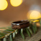 Dark wood ring made from ebony placed on pine needles, highlighting its natural texture and elegant curve.