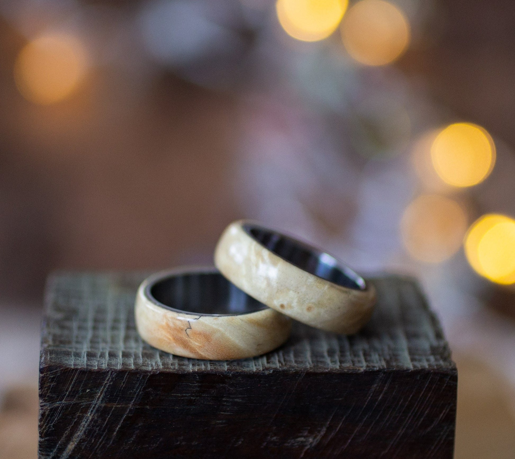 Pair of Andrwood Maple Wood Rings with Stainless Steel Core resting on wooden surface, ideal for matching couples or wedding bands.