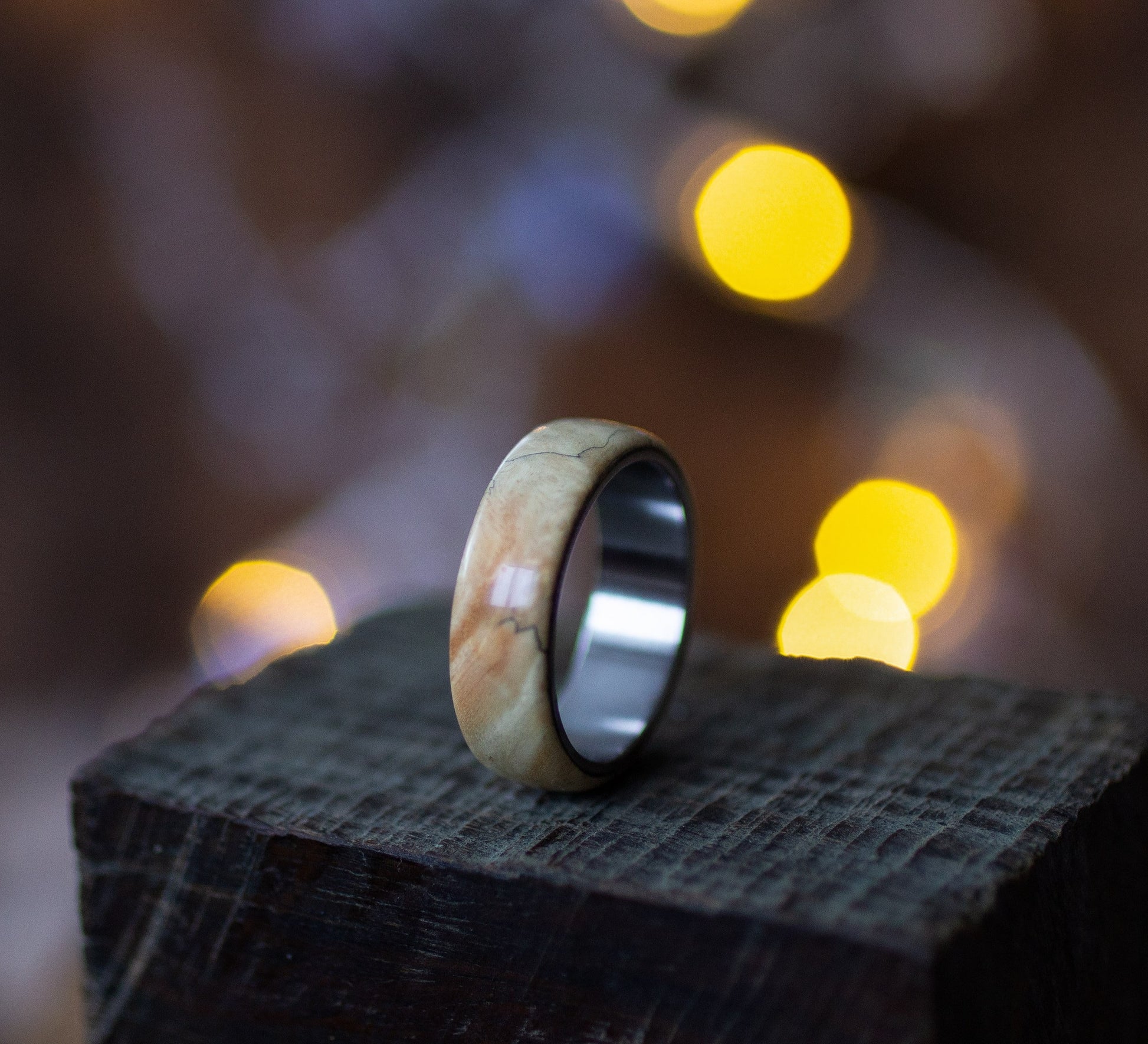 Close-up of Andrwood Maple Wood Ring with Stainless Steel Core on wooden block, emphasizing craftsmanship and minimalist design.