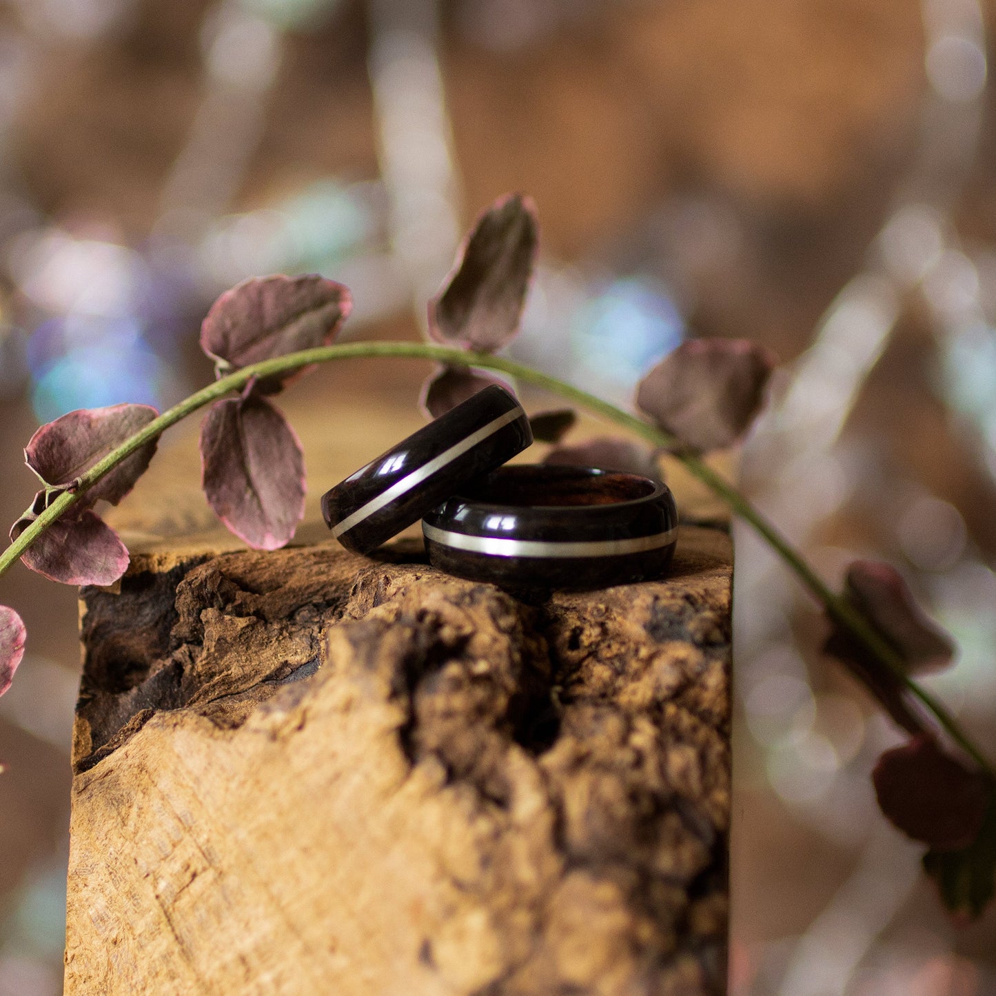Pair of Ebony Wood Rings with Silver Inlay by Andrwood resting on textured wood, ideal for couple promise rings or anniversary gifts.