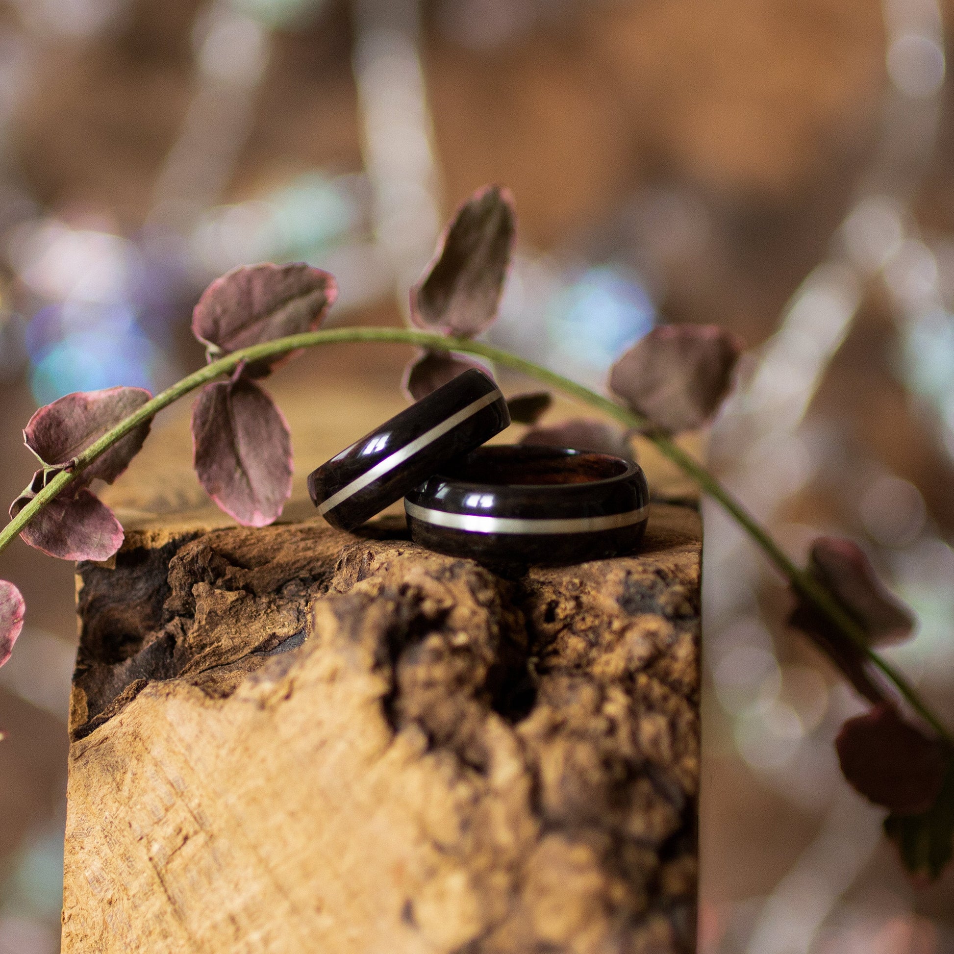 Pair of Ebony Wood Rings with Silver Inlay by Andrwood resting on textured wood, ideal for couple promise rings or anniversary gifts.
