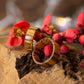 Pair of Zebrano wood rings beside blooming red buds, showing polished finish and golden wood tones.