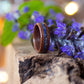 Makore and lapis lazuli ring resting on rustic wood, surrounded by purple blossoms.