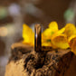 Ash wood ring with copper accents beside yellow flowers on rustic bark, showing grain and polish.