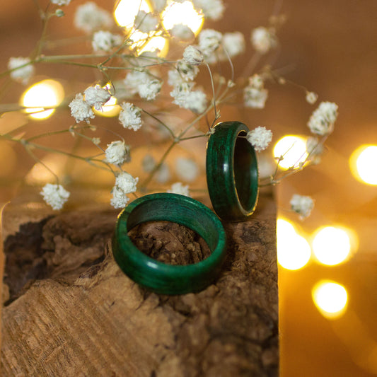 Pair of green-stained hornbeam rings on bark, styled with delicate white flowers and warm fairy lights.