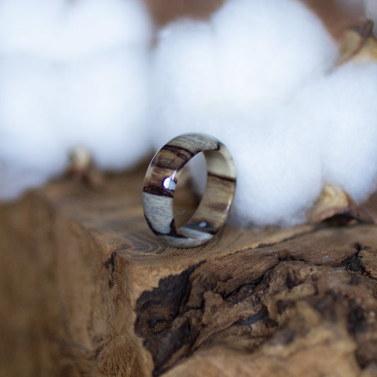 Epoxy birch wood ring resting on rugged bark with soft cotton tufts, highlighting its glossy finish.