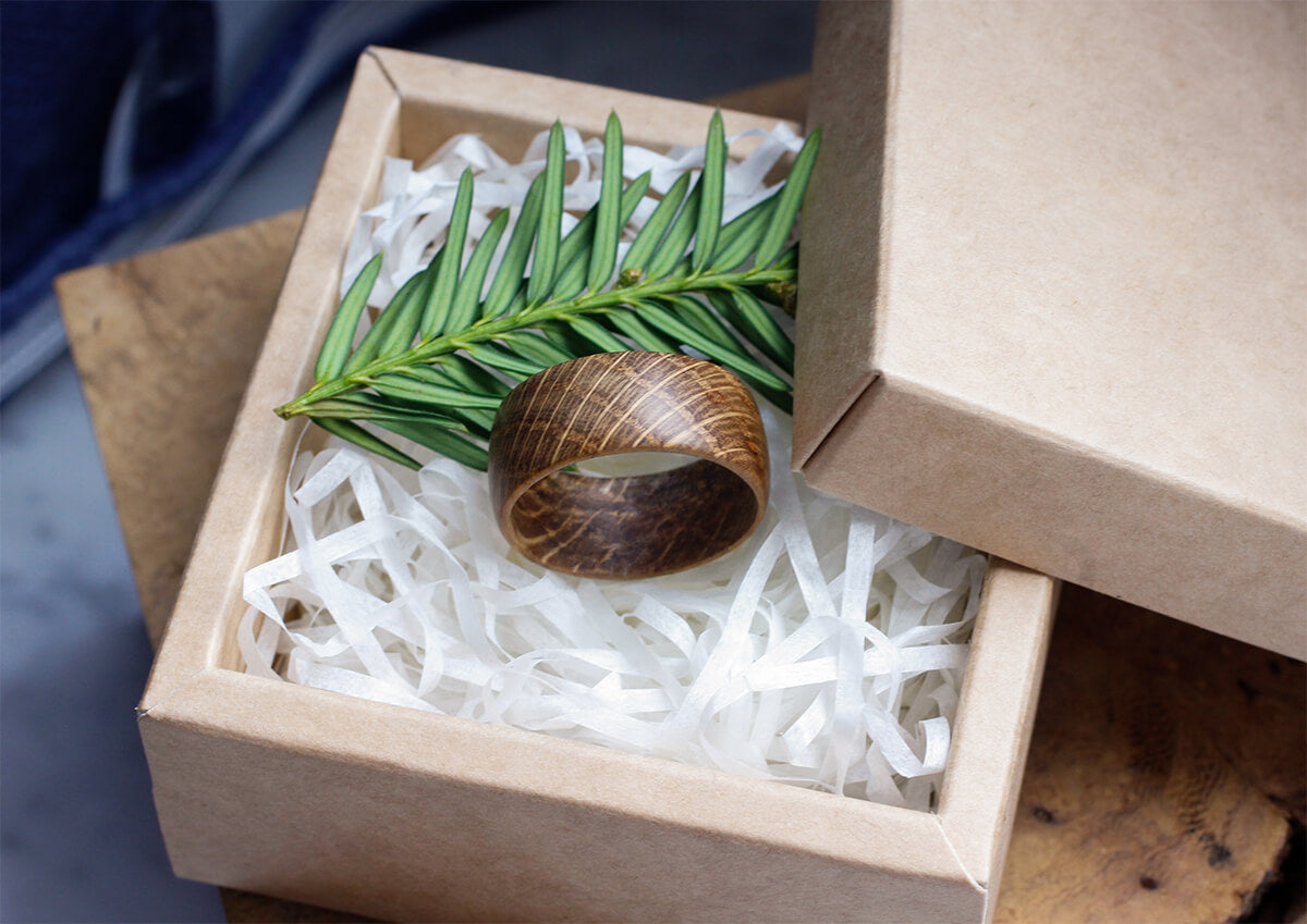 Wide oak wooden ring in eco-friendly gift box with green twig on shredded paper
