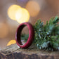 Glossy Purpleheart ring resting on bark with evergreen sprig, warm bokeh lights in the background.