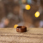 Single makore wood ring with warm reddish tone, lying flat on wood with cozy ambient lights.
