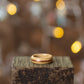 Ash wood ring with warm copper accent, placed on rustic dark wood under warm glowing lights.