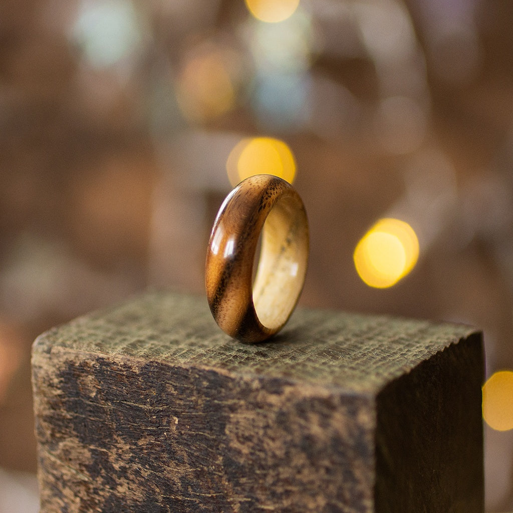 Striped ash wood ring with natural light and dark contrast, standing upright on rustic wooden block.