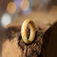 Maple burl wood ring with golden swirls and high-gloss finish, standing on rugged bark with soft light.