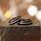 Pair of ebony rings with shimmering pearl inlay, placed flat on dark wood surface.