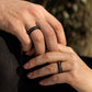 Close-up of couple holding hands, both wearing ebony rings with pearl inlay, soft light and earthy tone.