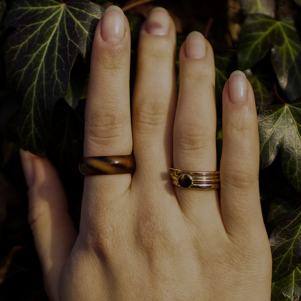 Hand wearing striped ash ring, fingers resting on ivy leaves in natural light.